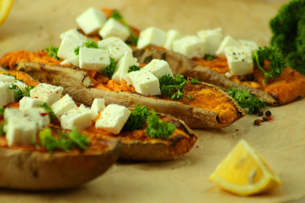 Süßkartoffeln mit Feta und einem Stück Zitrone auf Backpapier.