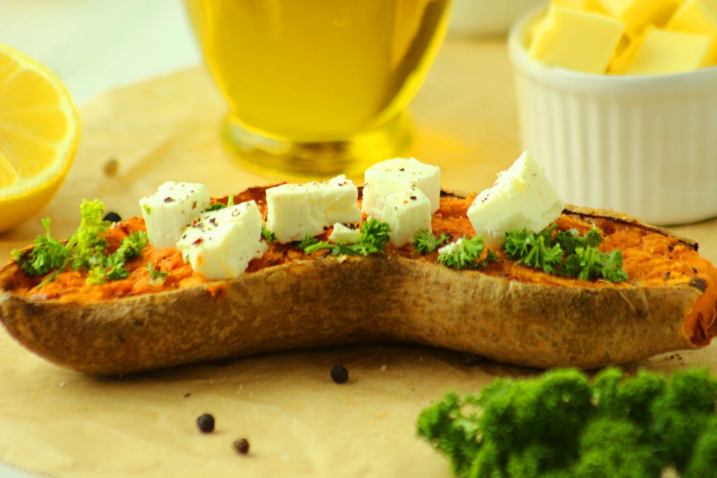 Eine Süßkartoffel mit kleinen Feta Stückchen belegt und einer Flasche Olivenöl im Hintergrund